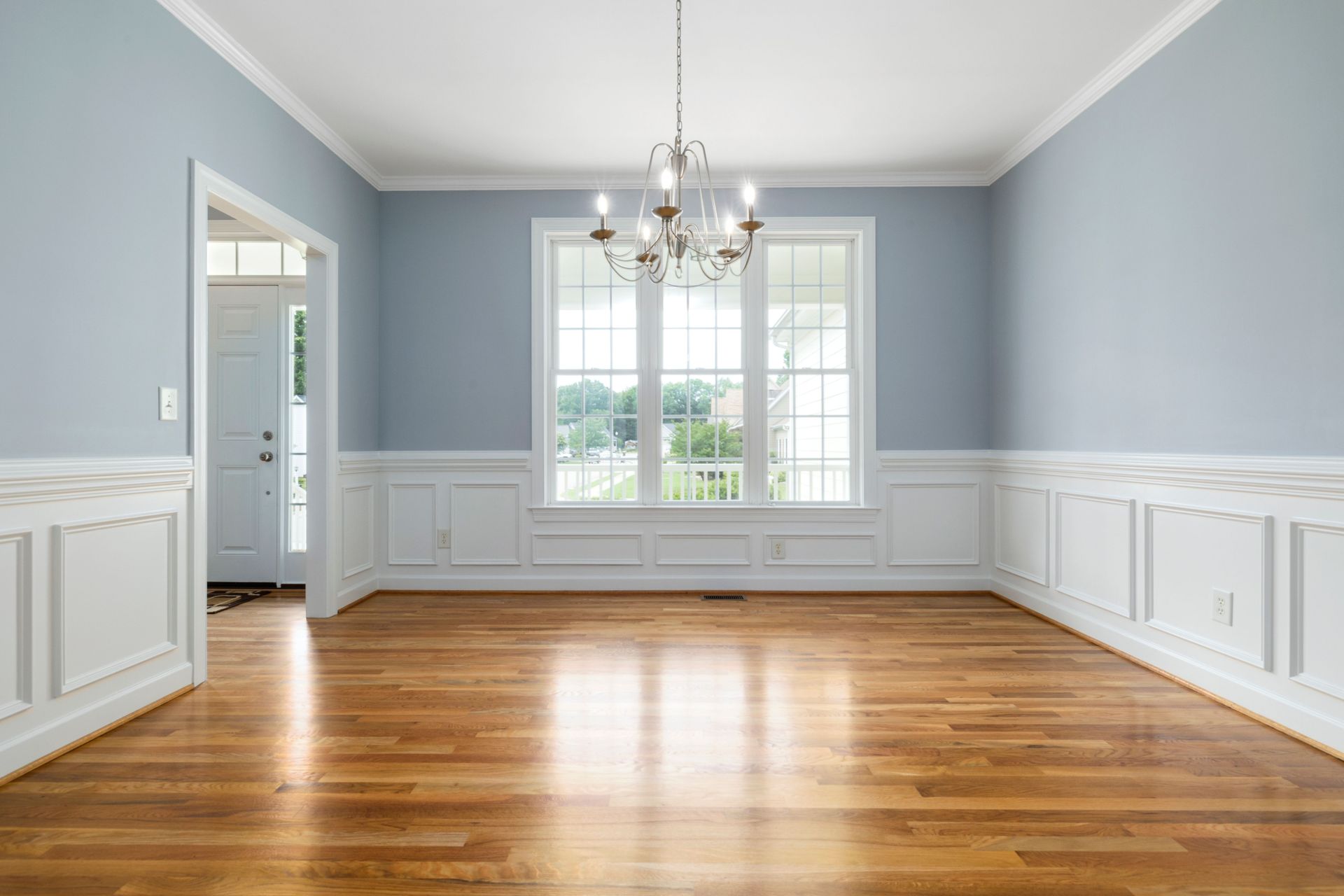 Bright empty room featuring a chandelier, wooden floor, and large windows.